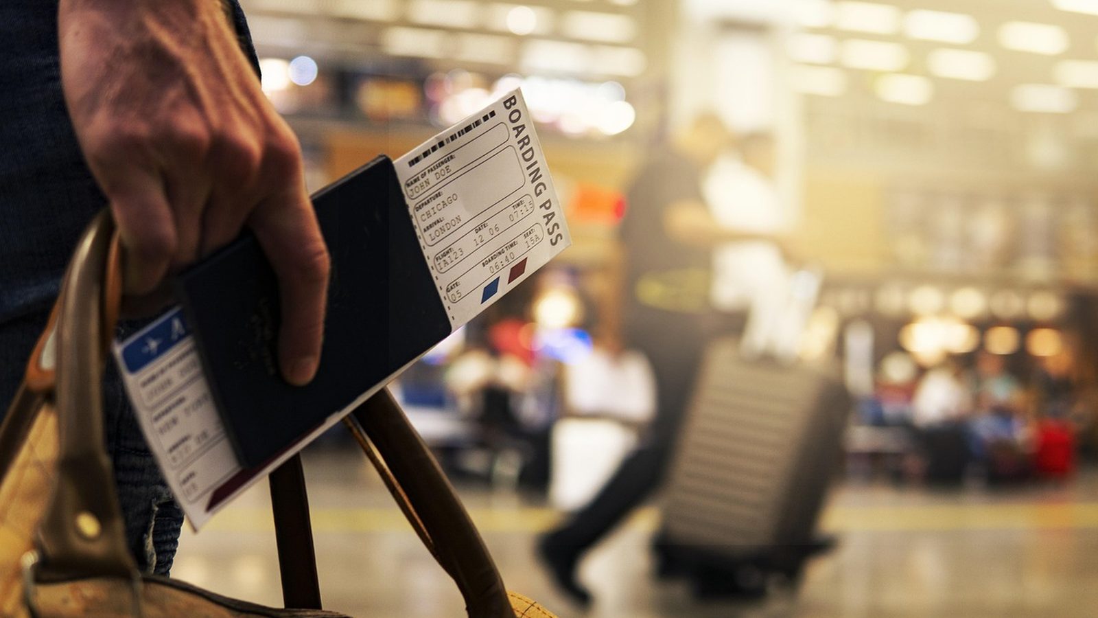 A traveller holding a passport and a boarding pass in an airport concourse